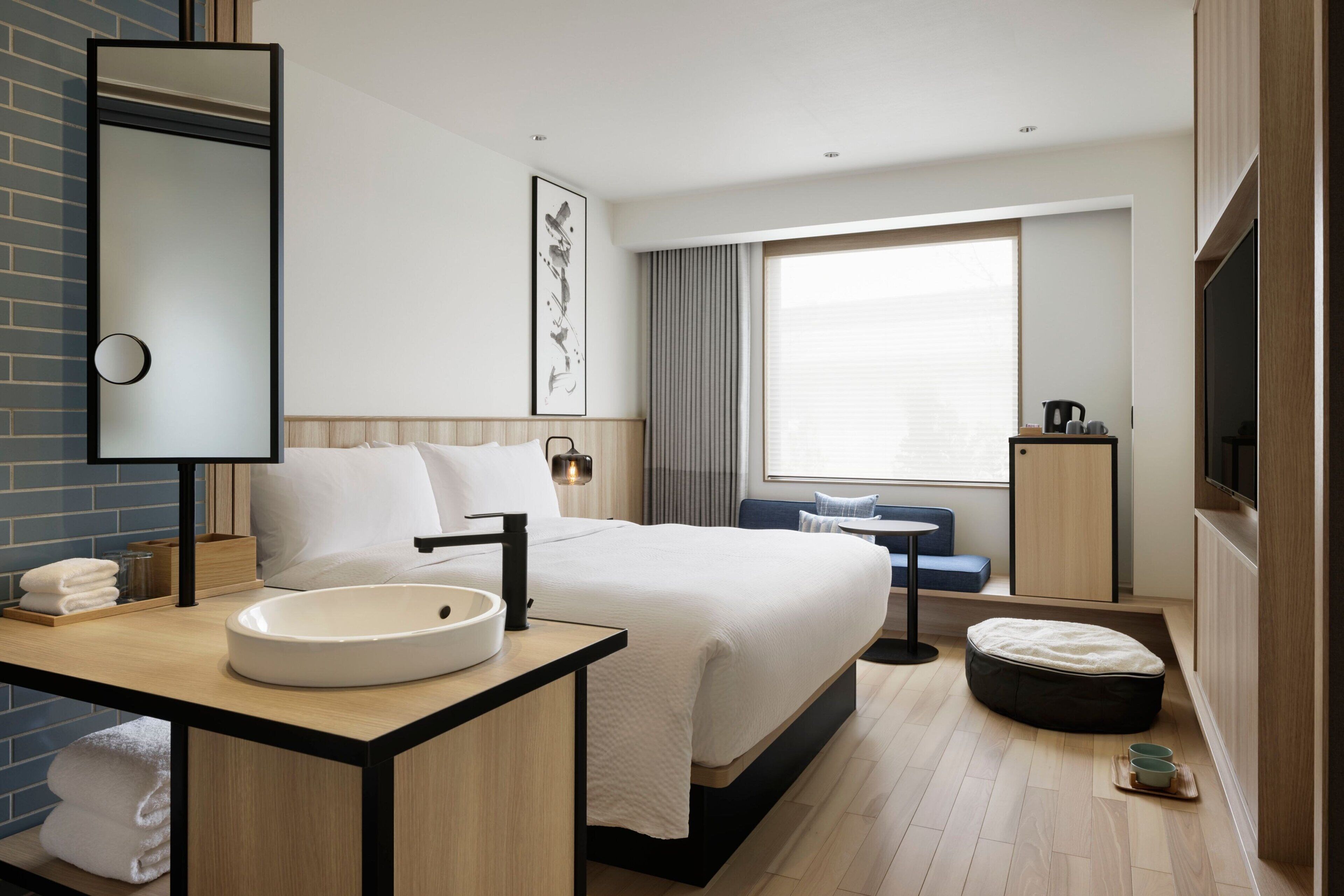 Habitació d'hotel moderna amb un llit gran, un lavabo rodó, un mirall, una televisió i una finestra amb cortines.