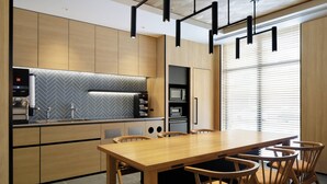 Eine moderne Küche mit Holzausbau, einer Fischgrät-Spritzschutzleiste und einem eingebauten Backofen. Ein Esstisch mit Stühlen und Pendelleuchten ist vorhanden.