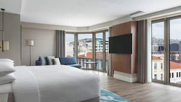 Une chambre d’hôtel moderne dotée d’un grand lit, d’un téléviseur à écran plat, d’une petite table et offrant une vue sur la ville grâce à de grandes fenêtres.