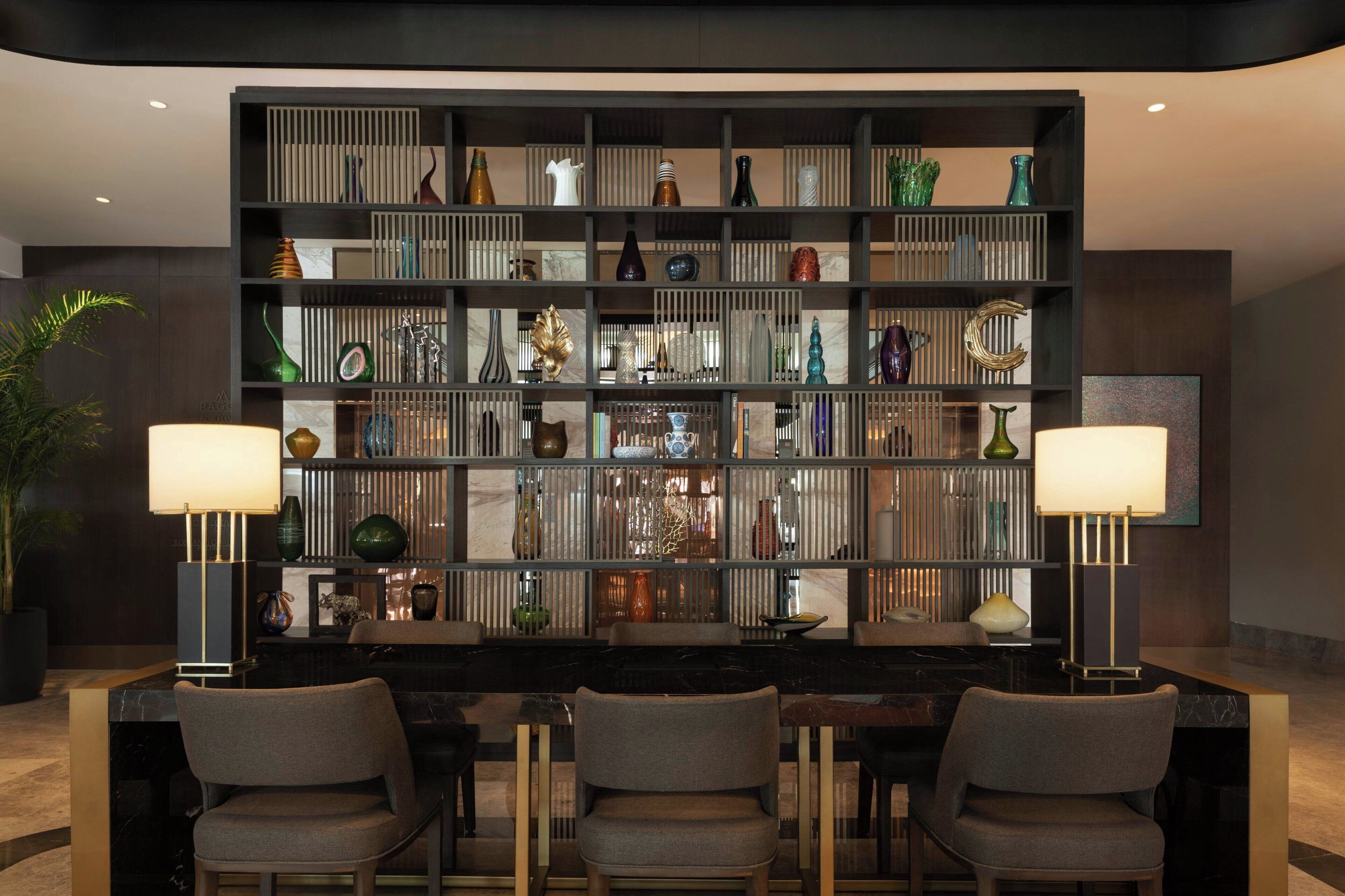 A modern interior with a black and white striped bookshelf, three chairs, and two table lamps.