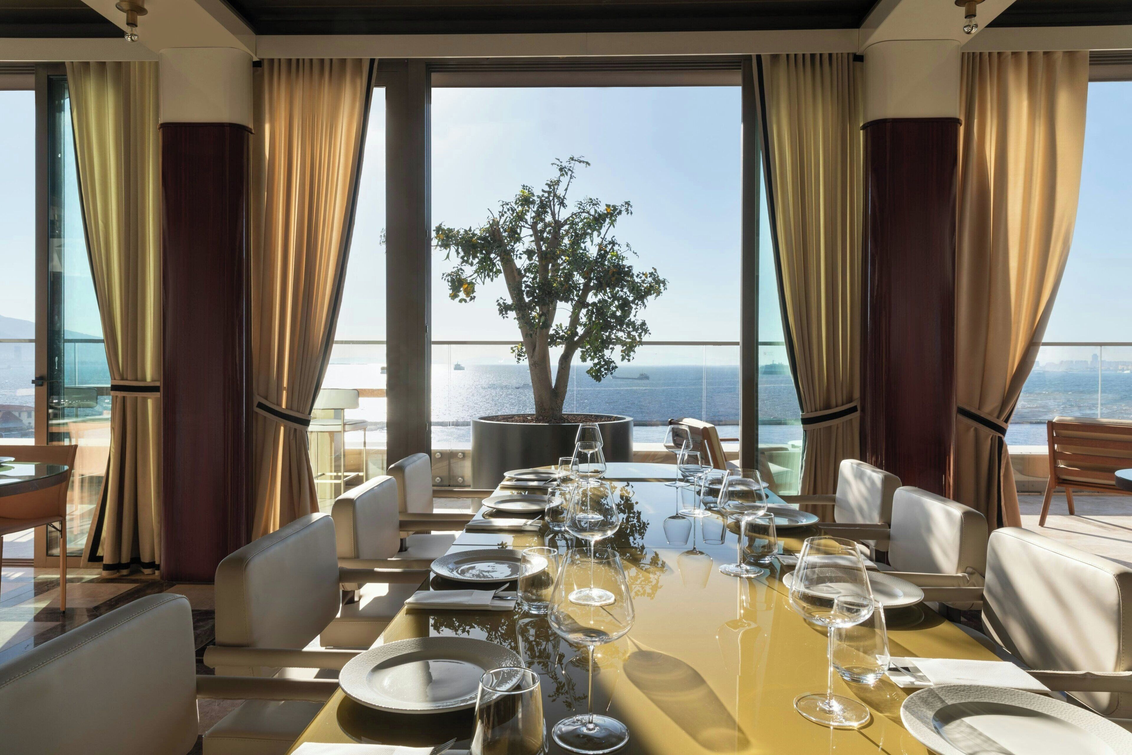 Comedor con mesa dispuesta para seis personas, ventanas amplias y vista al mar.