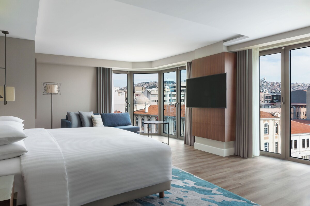 Een moderne hotelkamer met een groot bed, een flatscreen televisie en een balkon met uitzicht op de stad.