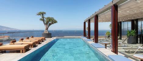 A rooftop infinity pool with lounge chairs and a view of the sea.