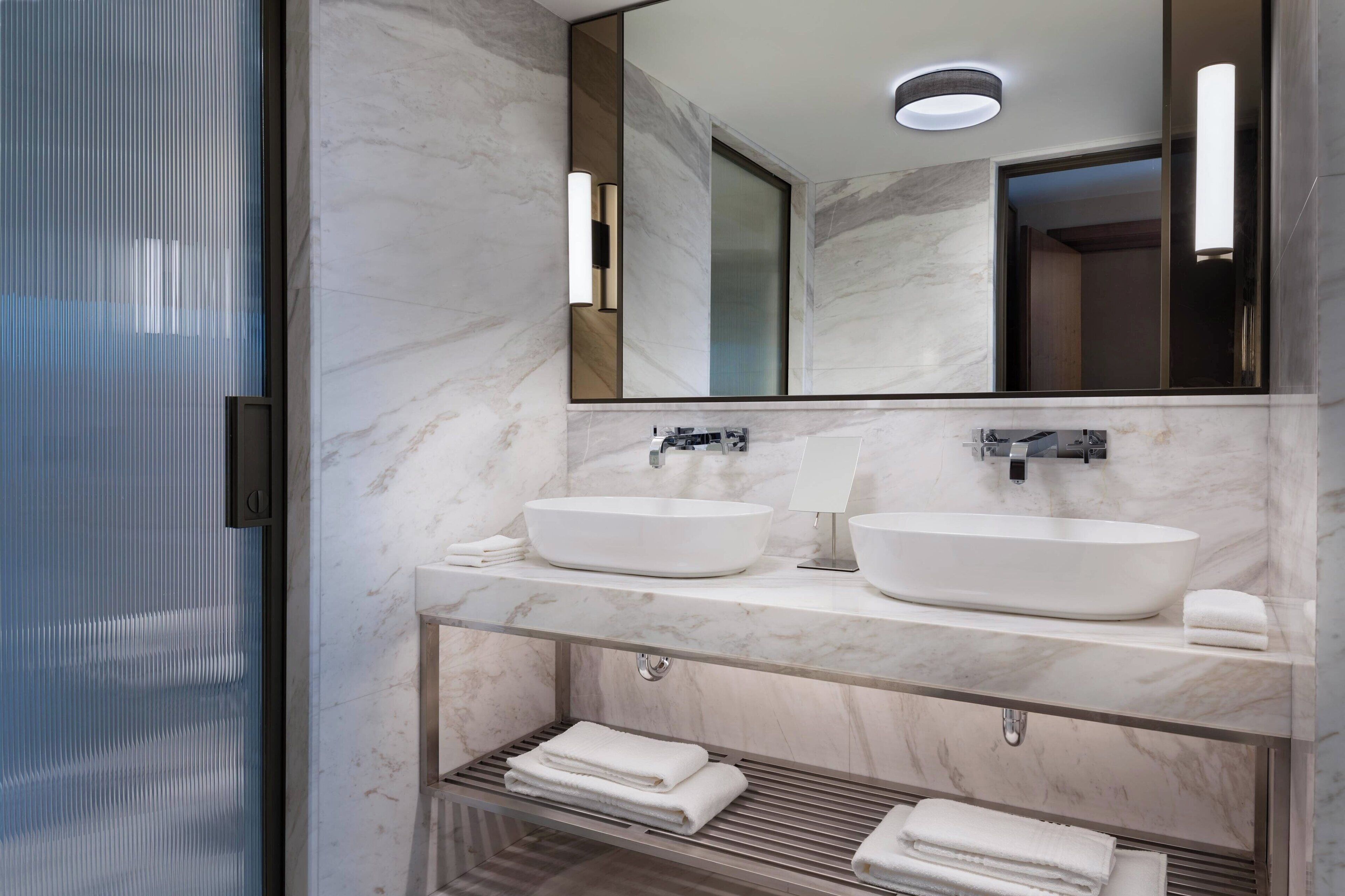 A modern bathroom with two sinks, a large mirror, and a towel rack.