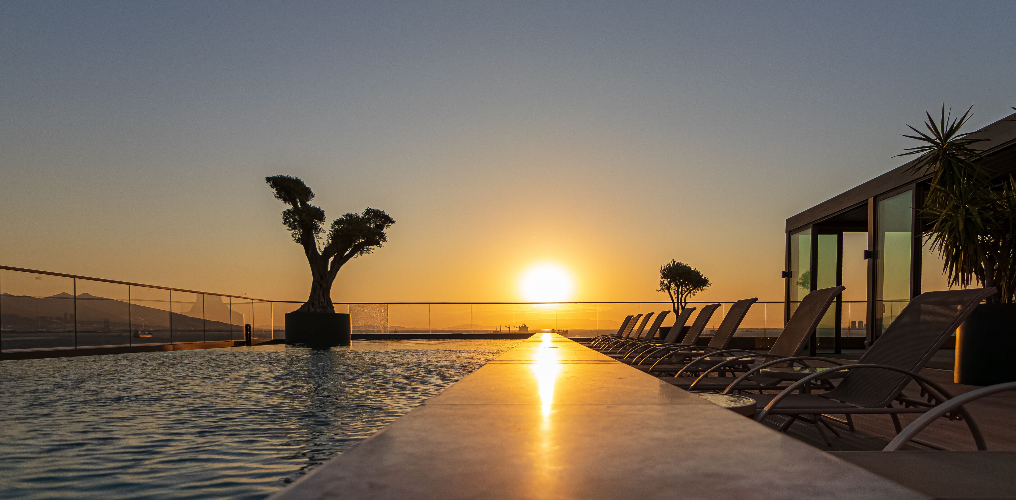 Ein Poolbereich mit Liegestühlen und Blick auf den Sonnenuntergang über dem Wasser.