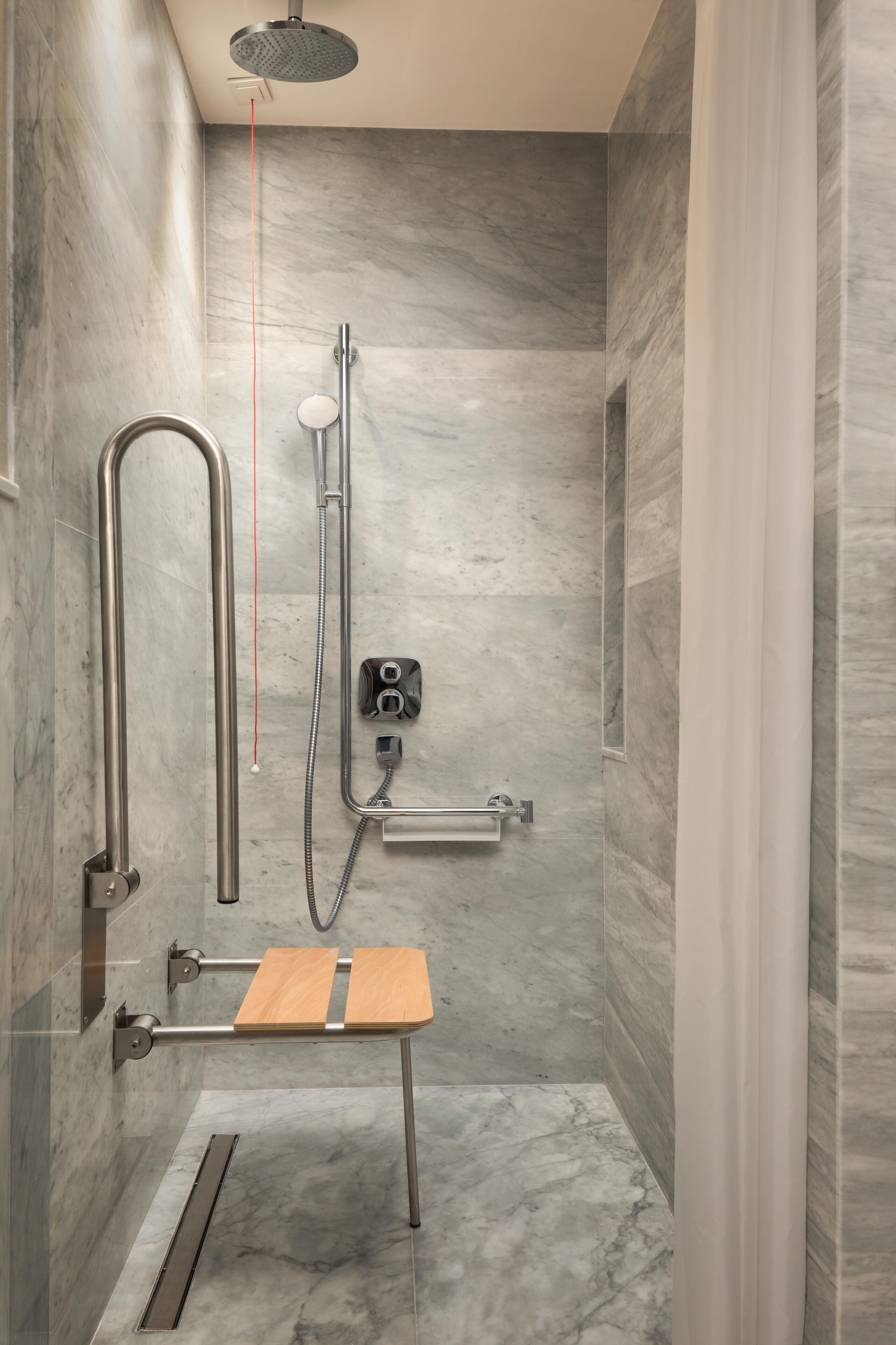Une douche moderne dotée d’un pommeau de douche à main, d’un flexible de douche et d’un siège en bois.
