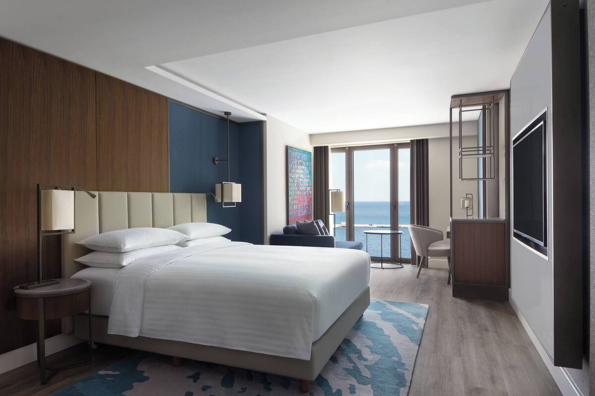 A modern hotel room with a large bed, a desk, a chair, and a view of the ocean.