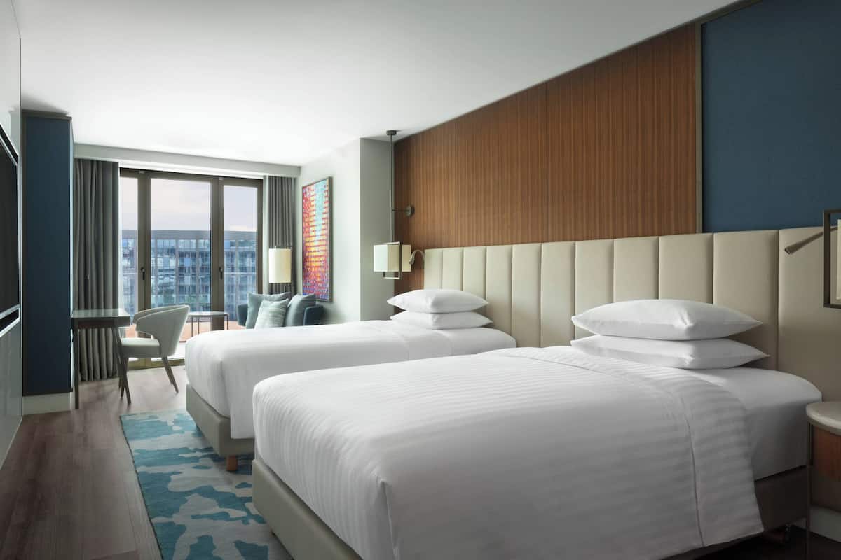 A hotel room with two beds, a view of the city, a desk, and a chair.