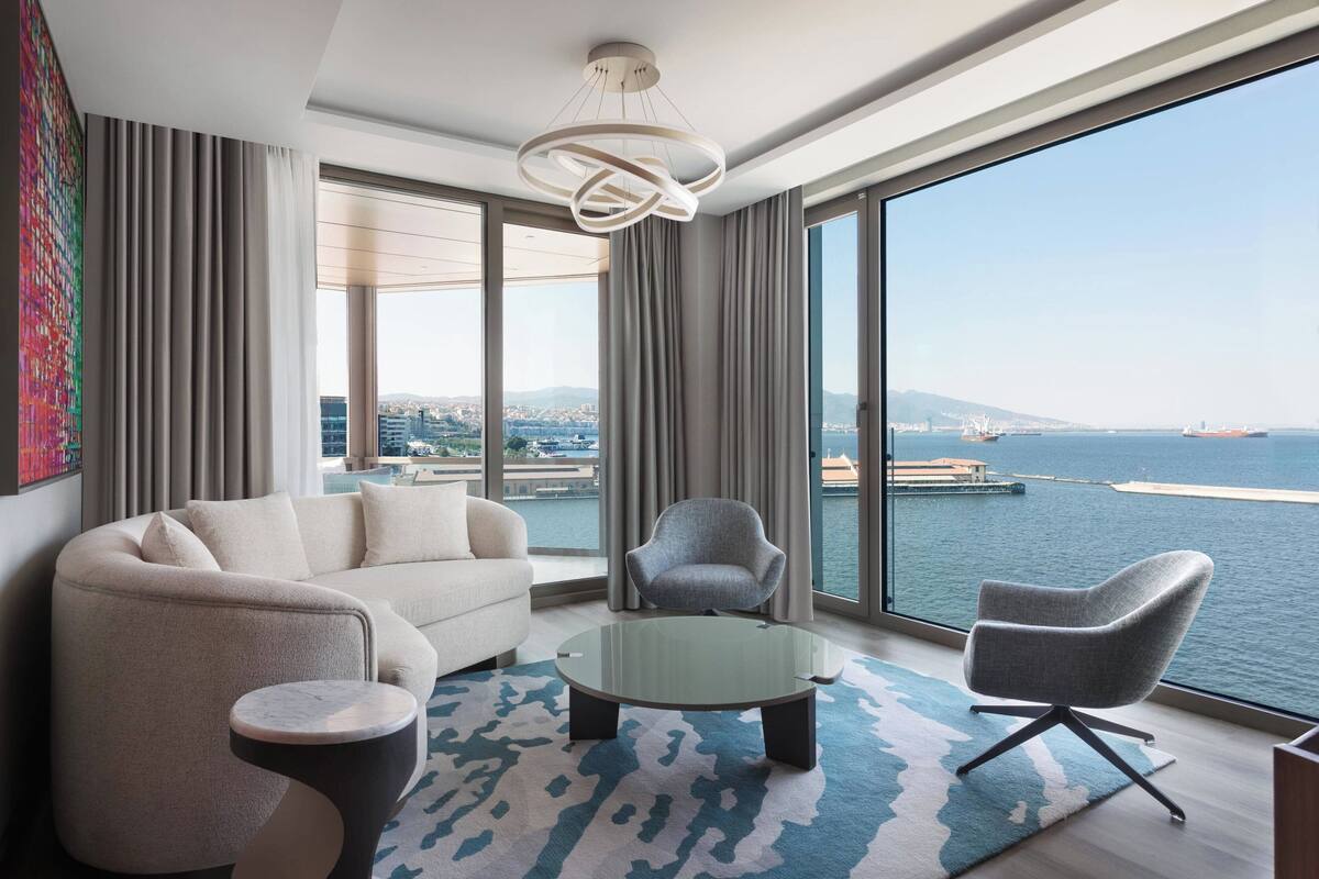 A modern living room with a sofa, armchairs, a coffee table, and a view of the sea.