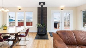 A modern living room with a fireplace, a dining area with a table and chairs, and a leather sofa. - Raven Lodge, Amazing Location and Epic Views, Sleeps 10 (Seward)