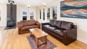 A living room with two brown leather sofas, a wooden coffee table, and a large painting on the wall. - Raven Lodge, Amazing Location and Epic Views, Sleeps 10 (Seward)