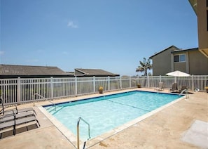 A rectangular swimming pool with a white fence, lounge chairs, and a palm tree in the background.