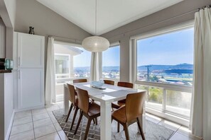 Un comedor con mesa y sillas, ventanas amplias que ofrecen vistas de la ciudad y una lámpara colgante.
