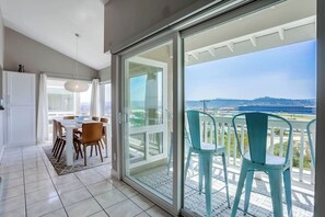 Un interior moderno con comedor, una puerta corrediza de vidrio que da a un balcón con sillas y vistas a la ciudad.