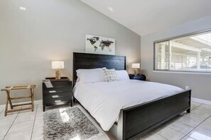 Un dormitorio moderno con una cama grande, dos mesitas de noche, un cuadro de un mapa mundial y una ventana con persianas.