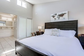 A modern bedroom with a large bed, a world map on the wall, and a bathroom visible through an open door.