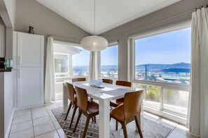 A dining area with a table and chairs, large windows with a view of a cityscape, and a hanging light fixture.