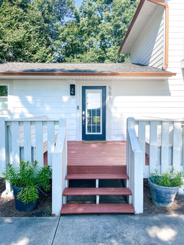 A white house with a dark blue door, a small porch with steps, and two potted plants.