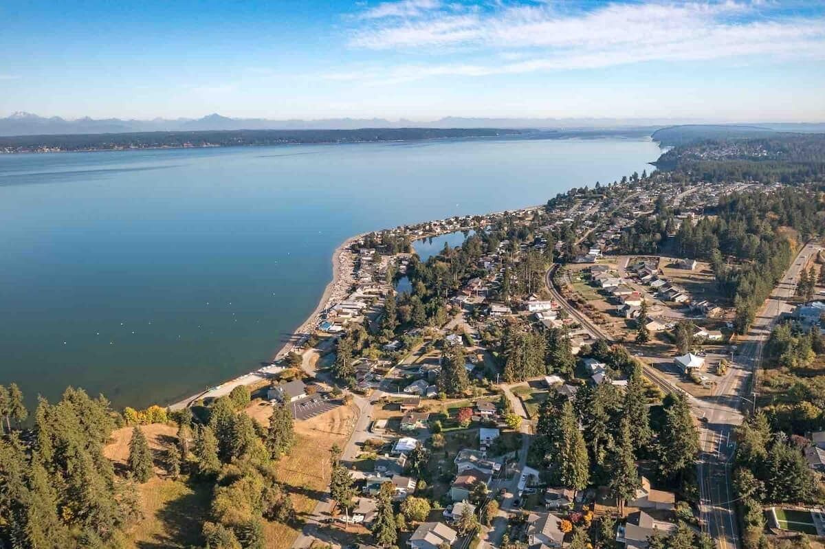 Vista aérea de un pueblo costero con un puerto deportivo, zonas residenciales y una gran extensión de agua.