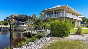 A waterfront property with a dock, boats, and a large house with a balcony and flag.
