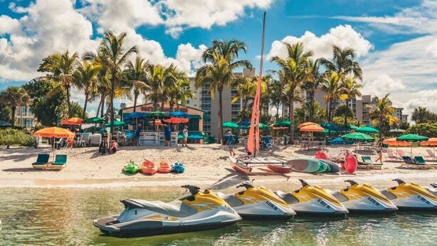 A beachside resort with jet skis lined up, palm trees, and colorful umbrellas.