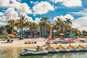 A beachside resort with jet skis lined up, palm trees, and colorful umbrellas.
