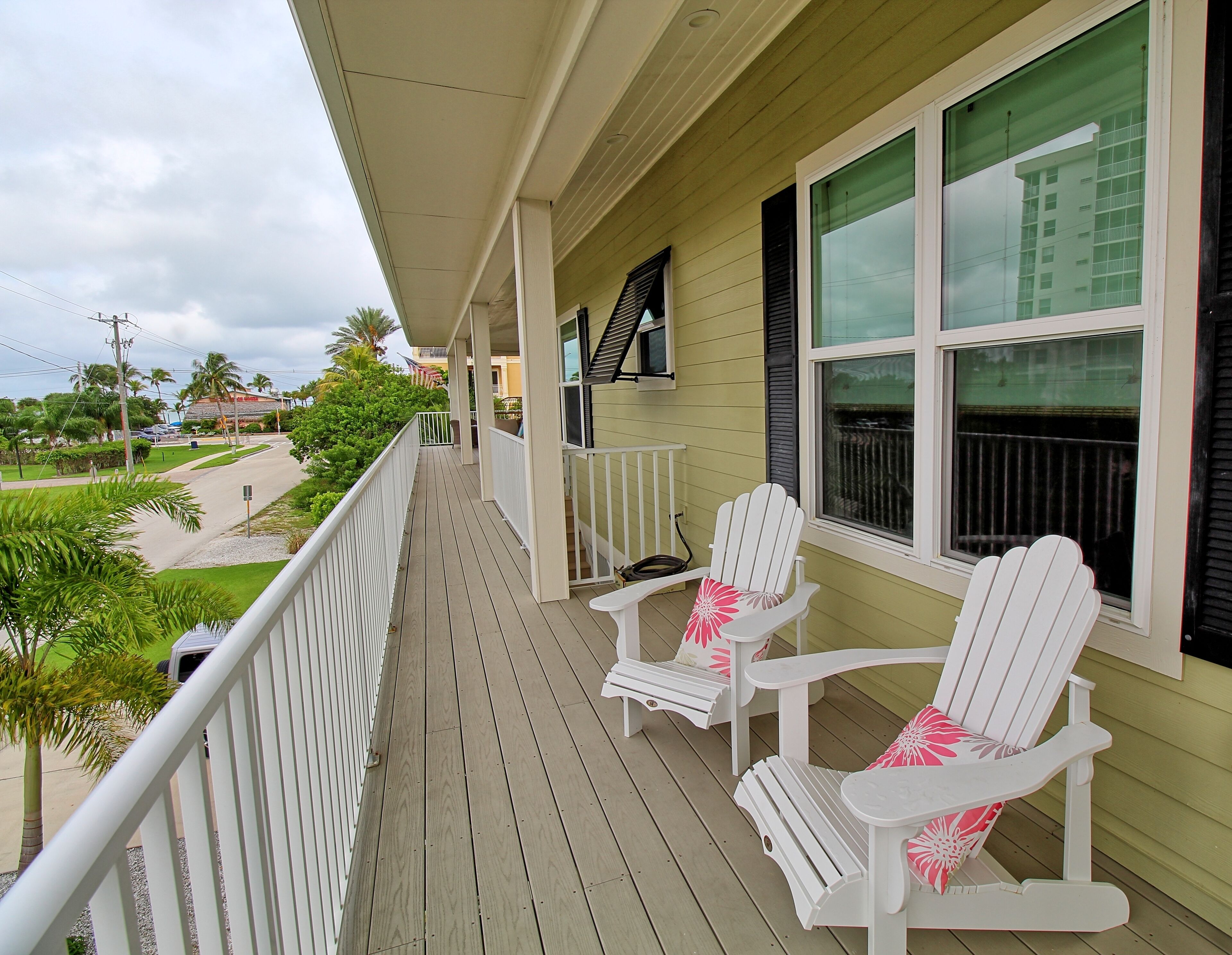 Un porche cubierto con sillas Adirondack blancas y vistas a una zona residencial.