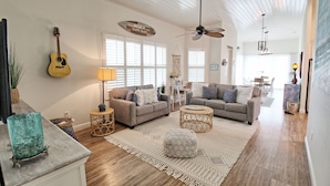 A spacious living room with a ceiling fan, two sofas, a coffee table, and a guitar on the wall.