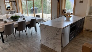 Una cocina moderna con una isla de mármol, piso de madera y ventanas amplias que ofrecen vistas al exterior.