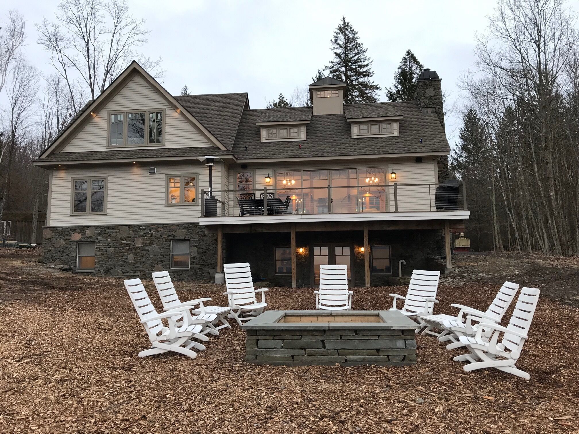 Une maison à deux étages avec une façade en pierre, un balcon doté d’un espace salon extérieur et un coin aménagé avec un foyer.