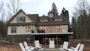 Una casa de dos pisos con fachada de piedra, un balcón con mobiliario exterior y una zona con fogata.