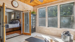 Ein Holzblock-Interieur mit Bett, großem Fenster, einer Uhr und einer Yogamatte.