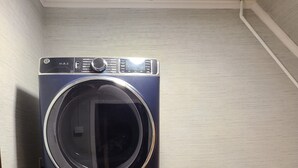 A stacked washer and dryer unit in a laundry room with a wooden floor and a couch with pillows in the background. - Midway between Saratoga Springs and Lake George (Glens Falls)