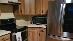 A kitchen with wooden cabinets, a stainless steel refrigerator, a microwave, an oven, and a coffee maker. - Midway between Saratoga Springs and Lake George (Glens Falls)