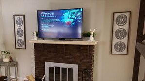 A living room with a fireplace, a television on top, and decorative wall art. - Midway between Saratoga Springs and Lake George (Glens Falls)