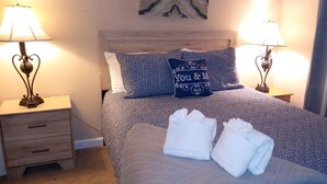 A neatly made bed with a blue and white patterned bedspread, two pillows, and two folded towels on the bed. There are two bedside tables with lamps and a small drawer. - The Zen Place<br>Weekly and Monthly discount (Hilton Head Island)