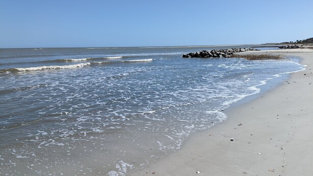A beach with calm waves, a sandy shore, and a distant rocky outcrop. - The Zen Place<br>Weekly and Monthly discount (Hilton Head Island)