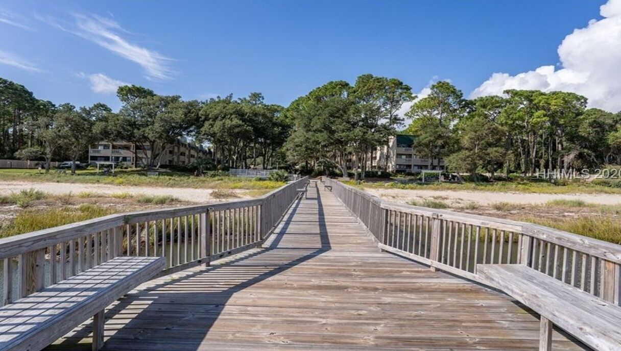 A wooden boardwalk leading to a building complex surrounded by trees.