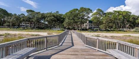 A wooden boardwalk leading to a building complex surrounded by trees.