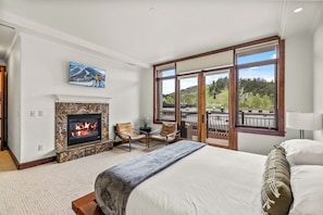 A bedroom with a fireplace, a bed, a TV, and a balcony with a scenic view.