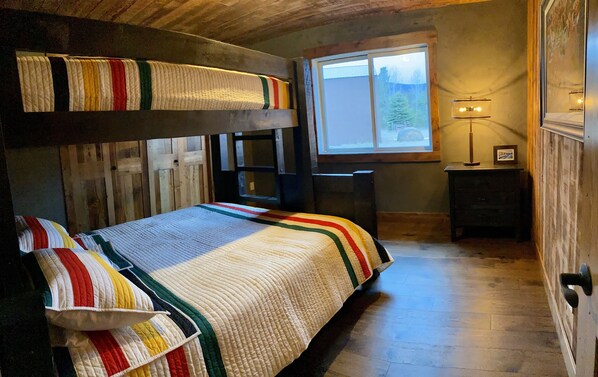 A cozy room with a bunk bed, a small desk, a lamp, and a window with a view of trees.