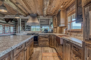 A rustic kitchen with wooden cabinets, granite countertops, and a large island. - Luxury Homestead Cowboy Cabin on 80 acres! (Whitefish)