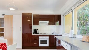 A modern kitchen with dark brown cabinets, white appliances, and a large window with a view of greenery. - Les Coccinelles by Interhome (Cavalaire)