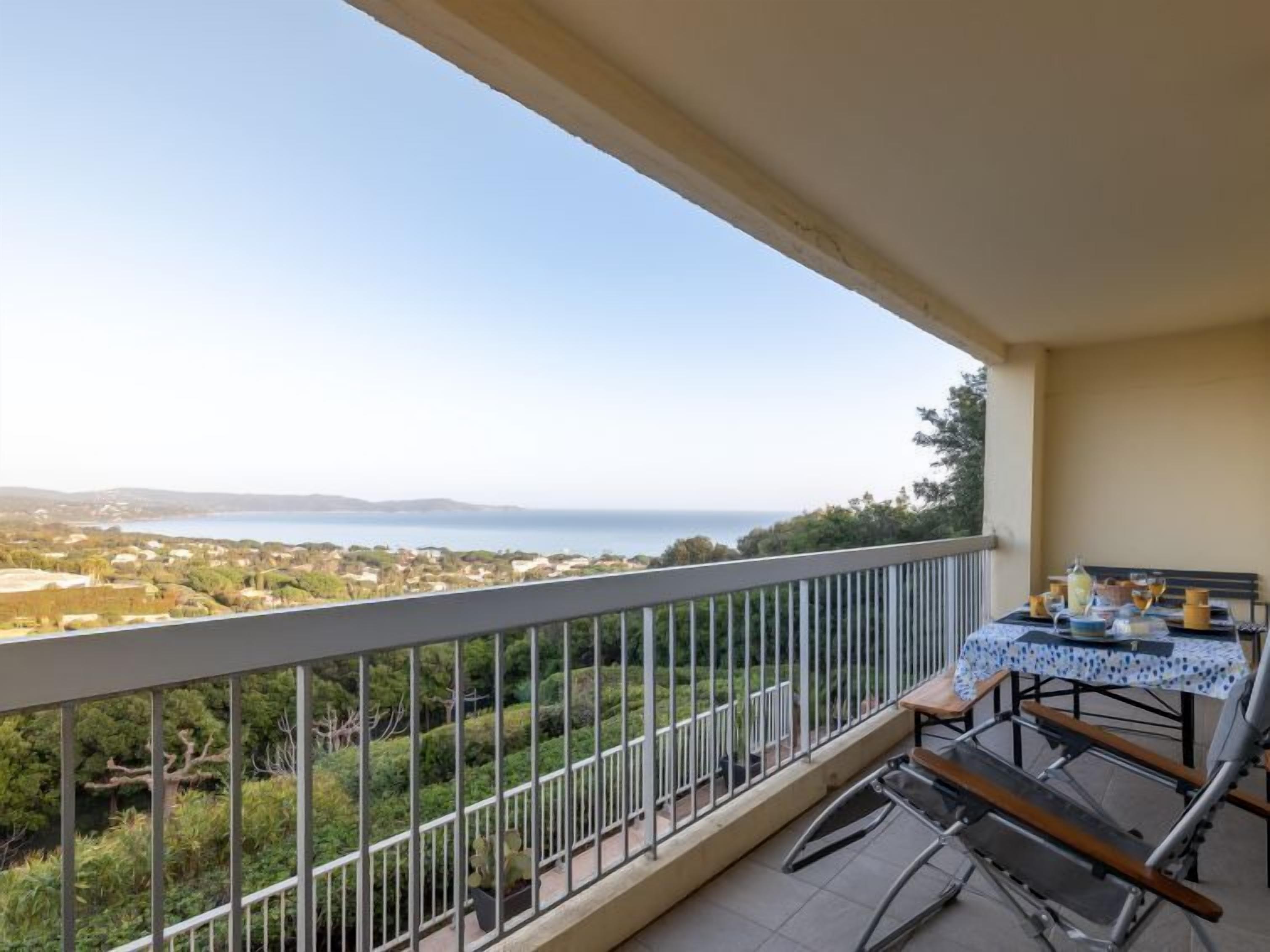 Varanda com mesa posta para refeições, com vista para uma paisagem costeira deslumbrante.