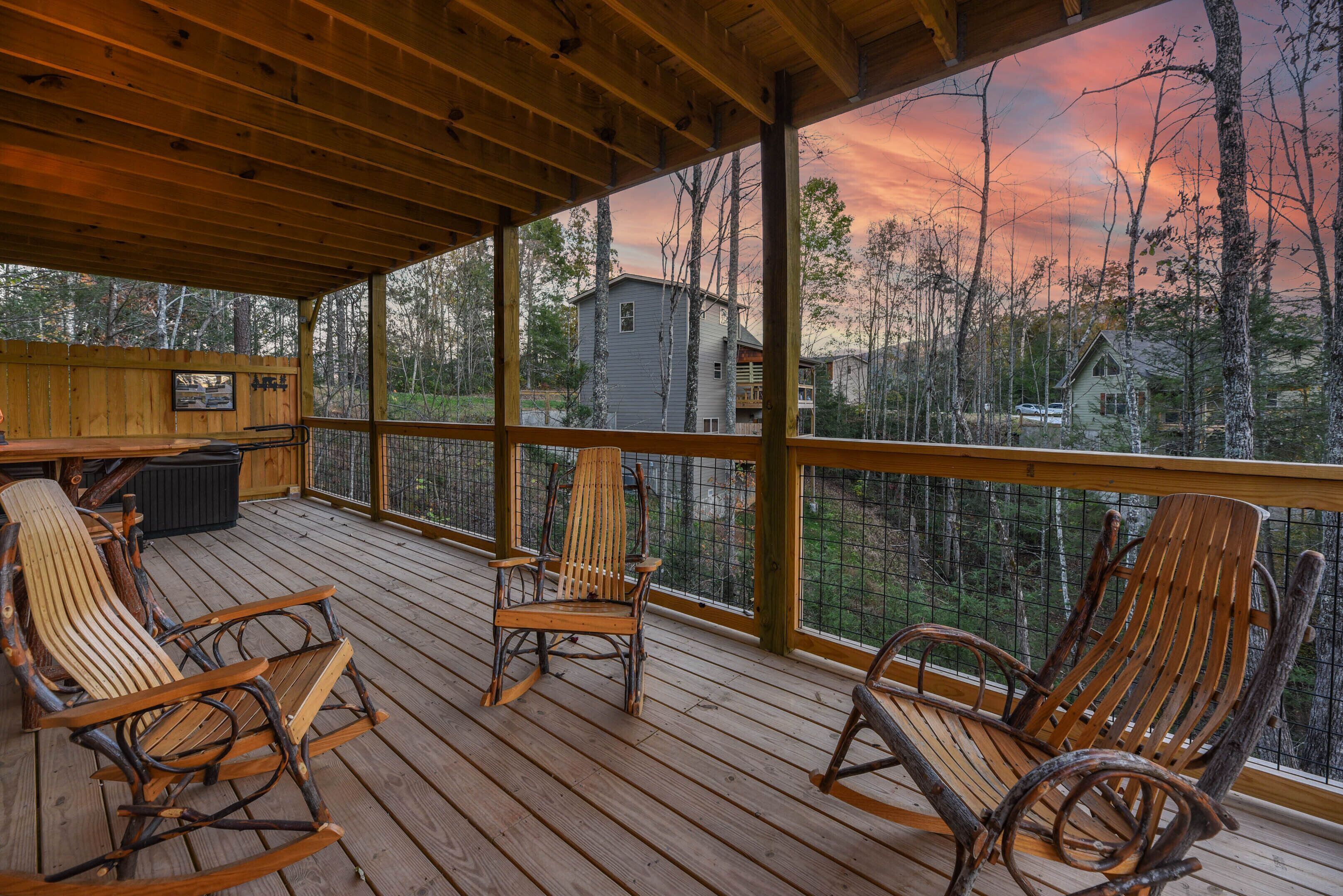 A wooden deck with rocking chairs and a view of a forested area.
