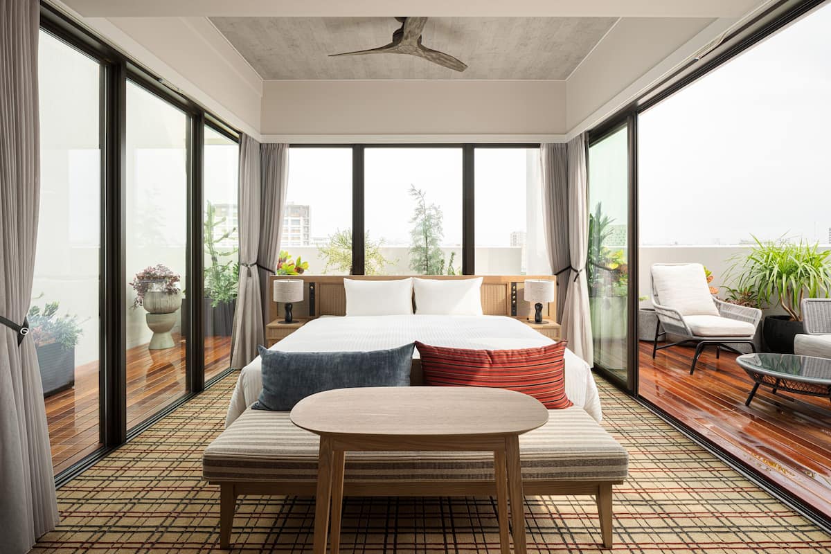 A modern hotel room with a large bed, a small table, and a balcony with seating.