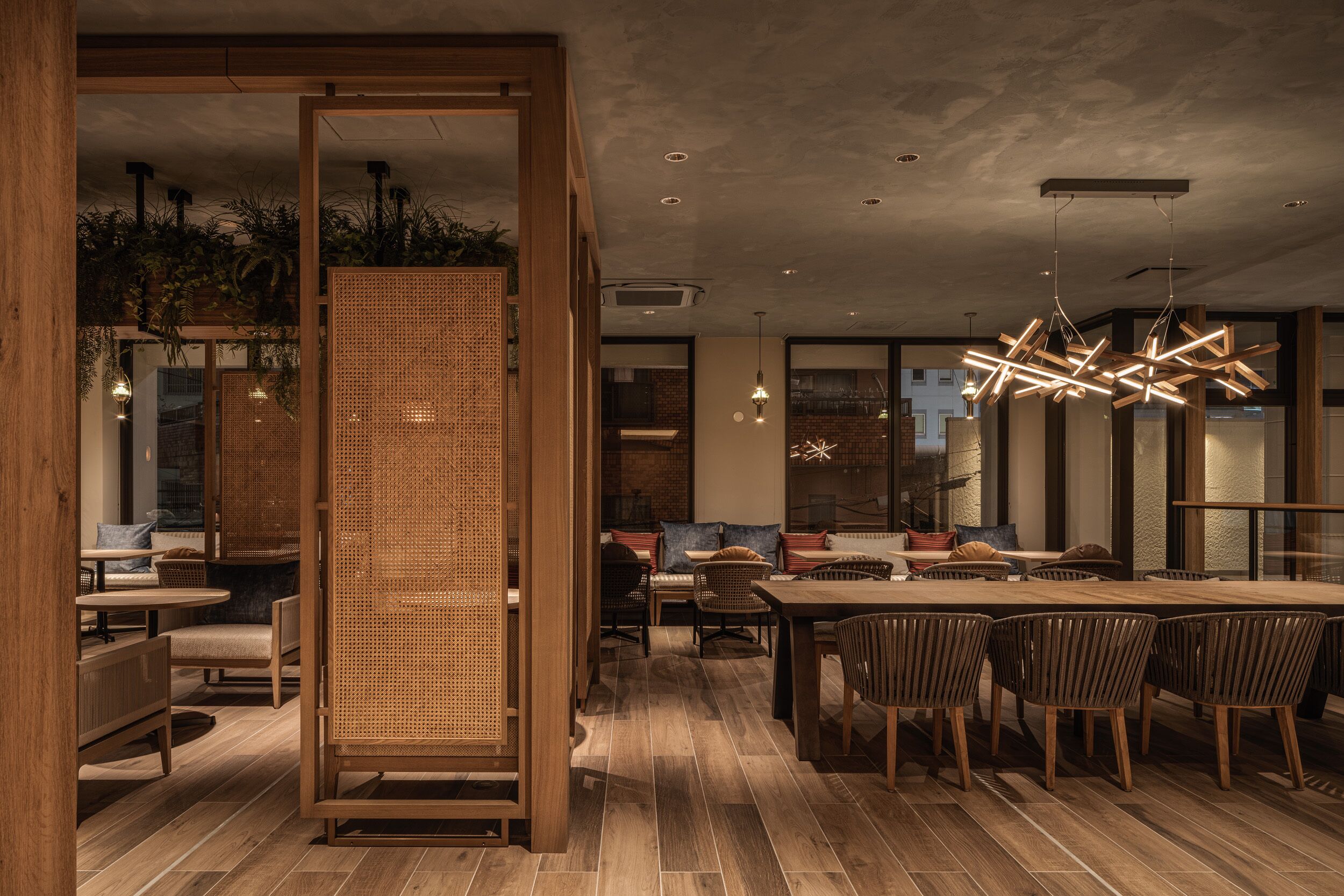 Un comedor moderno con una mesa y sillas de madera, un separador tejido e iluminación colgante.