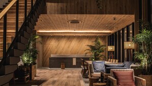 A modern interior with a wooden staircase, a seating area with sofas and a coffee table, and potted plants. - Nest Hotel Naha Kumoji (Naha)