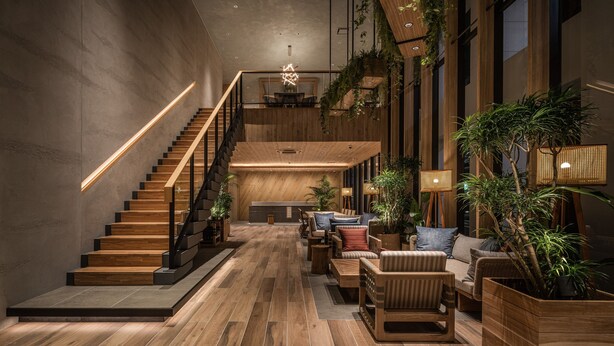 A modern interior with a wooden staircase, a lounge area with sofas and tables, and a kitchen in the background. - Nest Hotel Naha Kumoji (Naha)