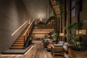A modern interior with a wooden staircase, a lounge area with sofas and tables, and a kitchen in the background. - Nest Hotel Naha Kumoji (Naha)